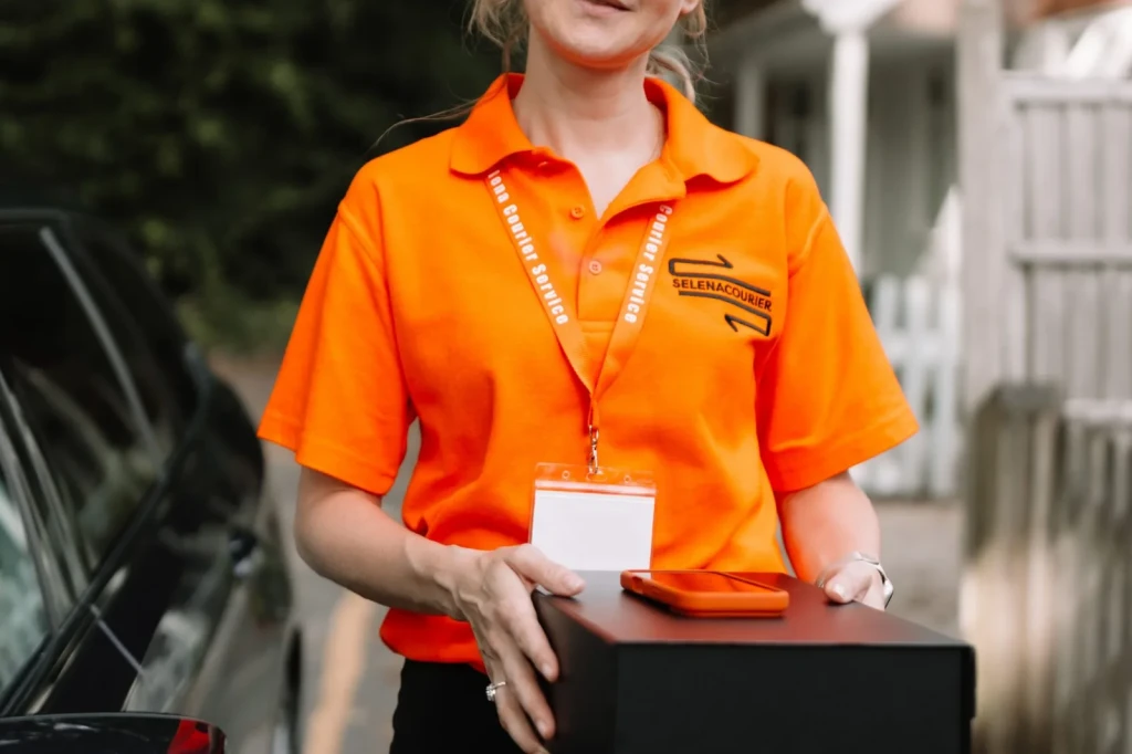 Selena courier in orange uniform carrying a branded delivery box
