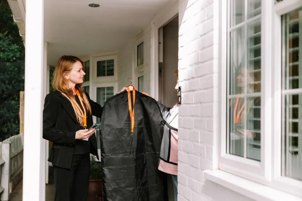 Selena courier handing a garment in a protective cover to a client