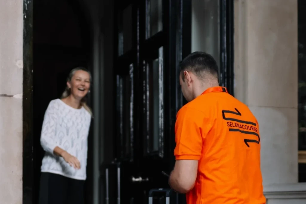 Selena courier arriving with luggage at a London townhouse as the recipient greets him at the door