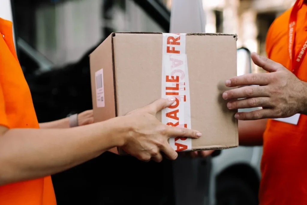 Two Selena Courier team members passing a parcel marked fragile between them beside a delivery vehicle