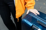 A courier's hand rests carefully on a navy hard-shell suitcase