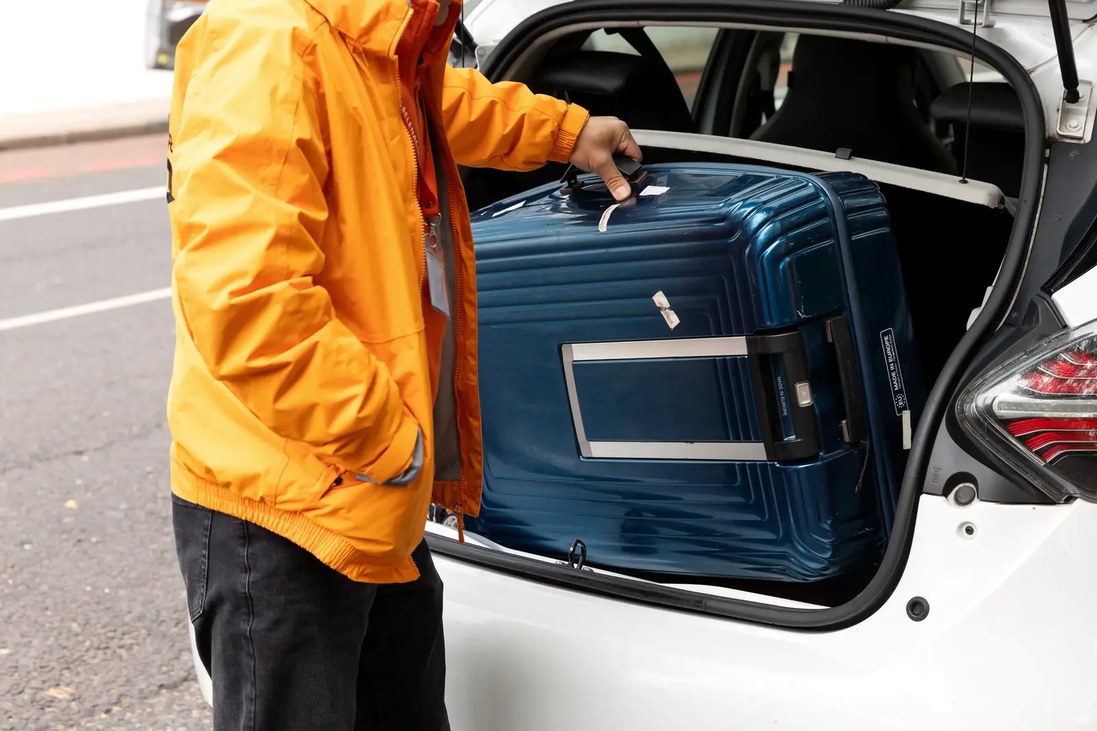A Selena courier lifts a navy suitcase into the boot of a car by its top handle