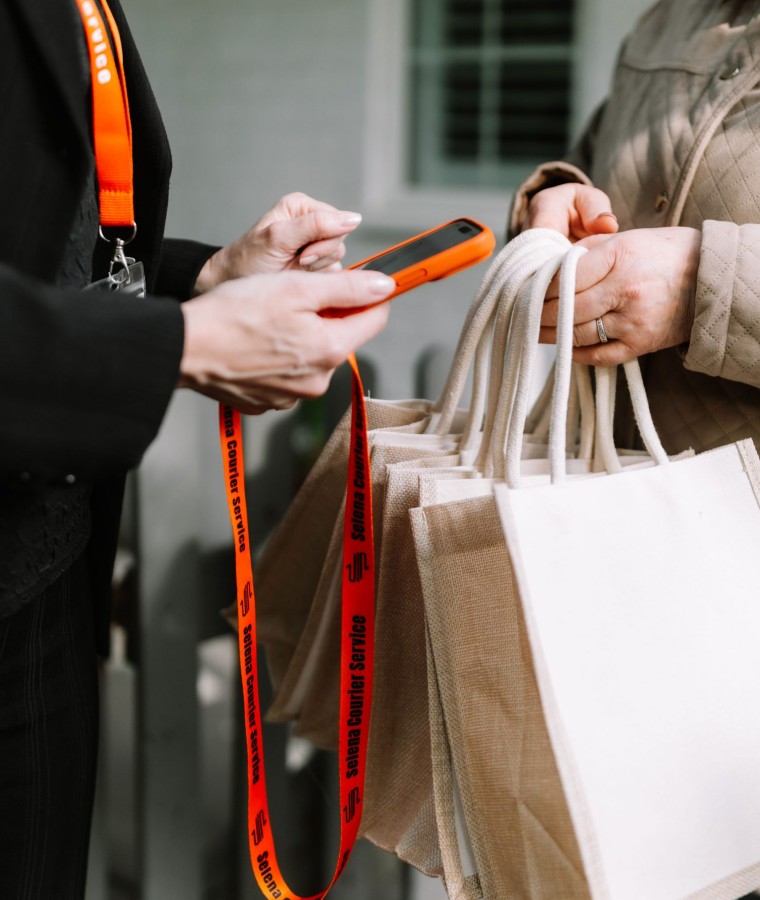 Selena courier handing over several prepared bags and confirming the delivery on a phone